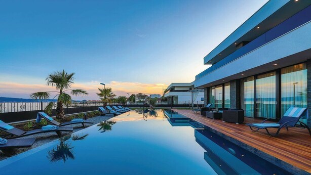 A modern hotel with a rooftop infinity pool, lounge chairs, and a view of the ocean at sunset. - Beachfront Villa Baronessa with Pool (Kastela)