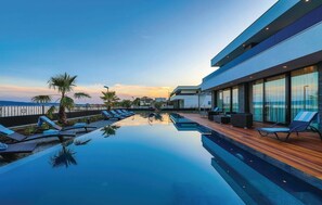 Ein modernes Hotel mit einem Dachpool, Liegestühlen und Blick auf den Ozean im Sonnenuntergang.
