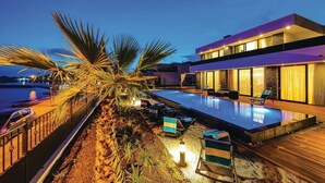 A modern poolside area with a pool, lounge chairs, and a building with large windows. - Beachfront Villa Baronessa with Pool (Kastela)