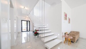 A modern interior with a staircase leading to an upper level, a small seating area with a table and cushions, and a door at the end of the hallway. - Beachfront Villa Baronessa with Pool (Kastela)
