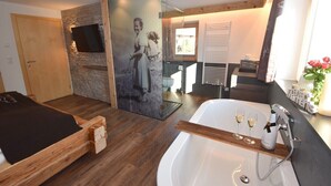 A modern bathroom with a large bathtub, a wooden bench, a stone wall, and a television mounted on the wall. - Comfort Chalet Mühle - SKI in/SKI out, Sauna-Jacuzzi - by "wachterhof" (Kaltenbach)