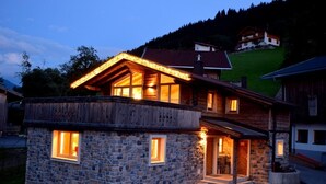 A two-story stone house with a wooden facade, large windows, and a well-lit entrance. - Comfort Chalet Mühle - SKI in/SKI out, Sauna-Jacuzzi - by "wachterhof" (Kaltenbach)