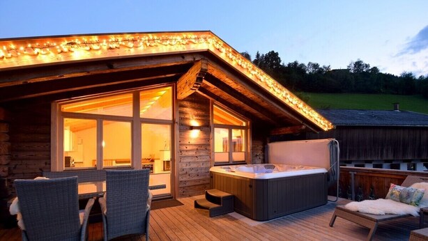 A wooden cabin with a hot tub, wicker furniture, and a deck. - Comfort Chalet Mühle - SKI in/SKI out, Sauna-Jacuzzi - by "wachterhof" (Kaltenbach)