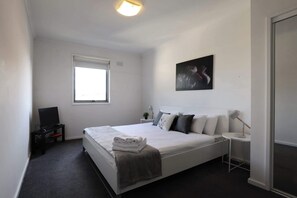 Une chambre à coucher avec un lit, un bureau, une chaise, une fenêtre, un tableau et une lampe.