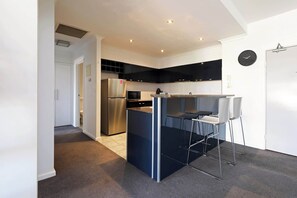 Cocina compacta con refrigerador integrado, microondas y pequeño comedor con mesa y sillas.