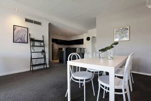 Une cuisine moderne équipée d’appareils électroménagers en acier inoxydable, un coin repas avec une table et des chaises blanches, et un espace de vie comprenant un canapé et une table basse.