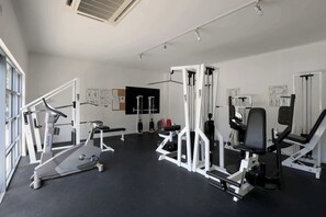 Un gimnasio con diversos equipos de ejercicio, incluyendo una cinta de correr, máquinas de pesas y una prensa de banca.