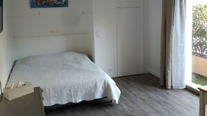 A bedroom with a bed, a painting, a wardrobe, and a window with curtains.