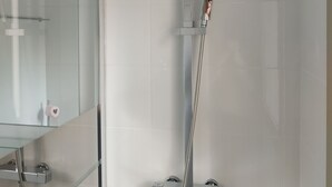 A modern bathroom with a glass shower enclosure, a large mirror, and a chrome showerhead.