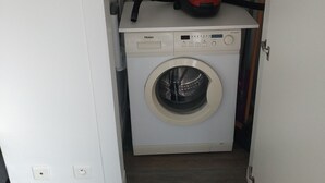 A compact laundry area with a front-loading washer and dryer, a red vacuum cleaner, and a white cabinet.