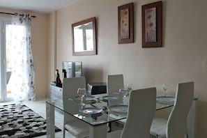 A dining area with a glass table, white chairs, and framed artwork on the wall.