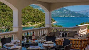 A dining area with tables set for a meal, overlooking a coastal landscape with mountains and a sea view. - Beachfront Villa Feodora Grande (Korcula)