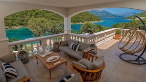 A terrace with a sofa set, a dining table, and a hanging chair, overlooking a turquoise sea and green hills. - Beachfront Villa Feodora Grande (Korcula)