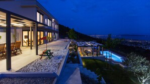 Une maison moderne dotée d’une piscine, d’un espace extérieur aménagé et offrant une vue sur la ville la nuit.