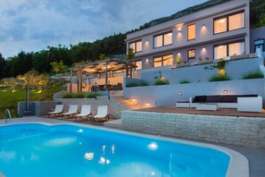 Una casa moderna con piscina, mobiliario exterior y un muro de contención de piedra.