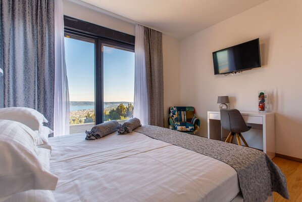 Habitación de hotel con una cama grande, un escritorio, una silla, un televisor y vistas a la ciudad.