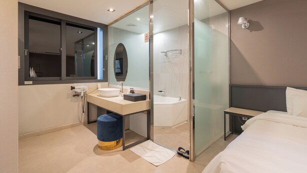 Una habitación de hotel moderna con ducha de vidrio, una cama grande, una mesita de noche y un televisor integrado.