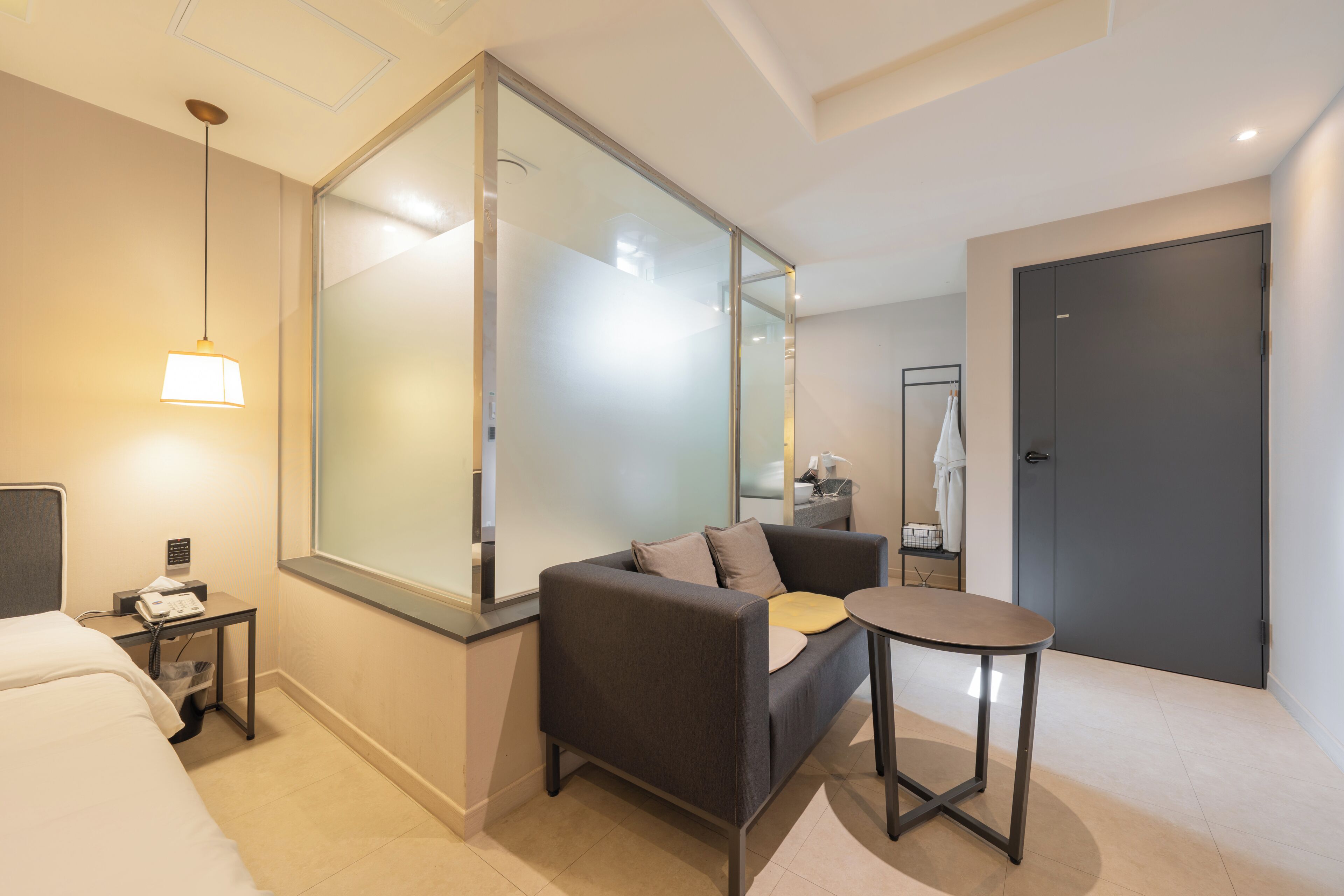 A modern hotel room with a bed, a sofa, a small table, a mirror, and a door.