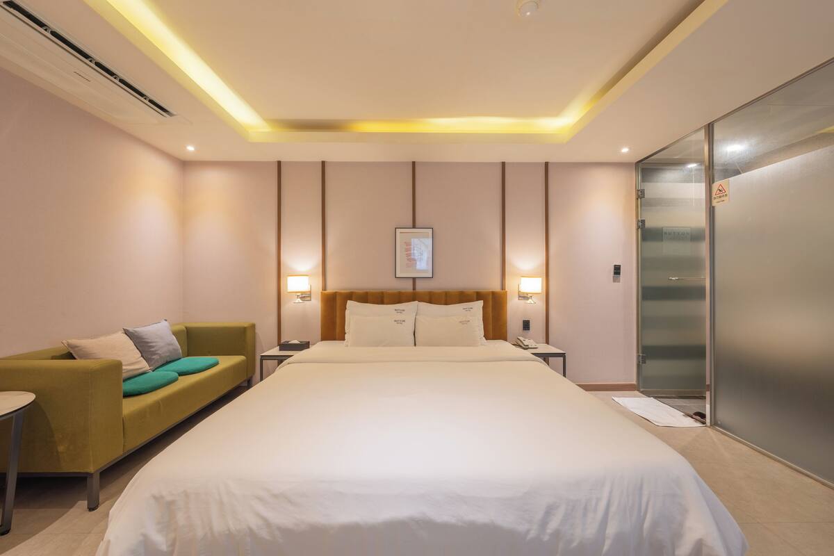 A hotel room with a large bed, a sofa, bedside tables, and a wardrobe.