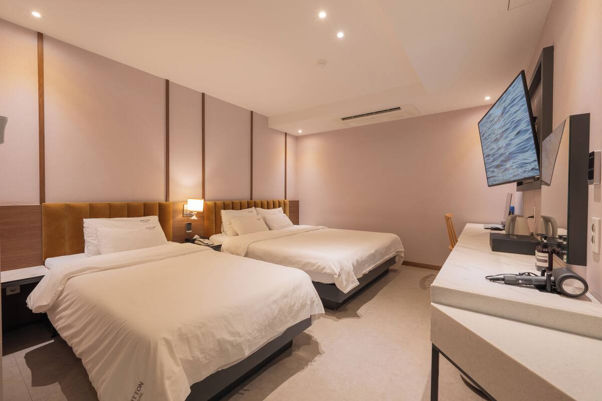 A hotel room with two beds, a desk with a computer, and a TV mounted on the wall.