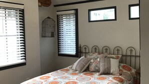 A bedroom with a large bed, a wooden chair, and a ceiling fan. There are two windows with blinds, and a wall-mounted birdcage. - Urban Chic Studio, Private, 1B1B.  Belhaven area.   Near campus& hospitals. (Jackson)