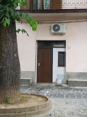 A building with a brown door, a small window, and an air conditioning unit mounted on the wall. - Casa Nostra (Ceraso)