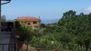 A house with a red roof, surrounded by greenery and hills in the background.