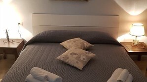 A neatly made bed with two pillows and rolled towels, a painting on the wall, and bedside lamps.