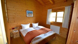 Un dormitorio de cabaña de madera con cama, mesita de noche, ventana con cortinas e imagen en la pared.