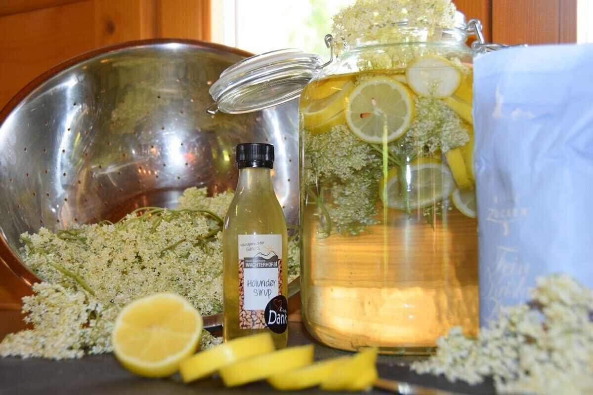 A kitchen with a stainless steel sink, a large glass jar with a lid, and a bottle of holunder syrup.
