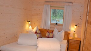A wooden cabin bedroom with a bed, pillows, a nightstand with a bottle, and a window with curtains. - Waldhütte - SKI in/SKI out - by "wachterhof" (Kaltenbach)