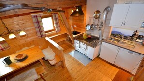 A cozy cabin interior with a wooden dining table, bench, and a kitchenette area with a sink and stove. - Waldhütte - SKI in/SKI out - by "wachterhof" (Kaltenbach)