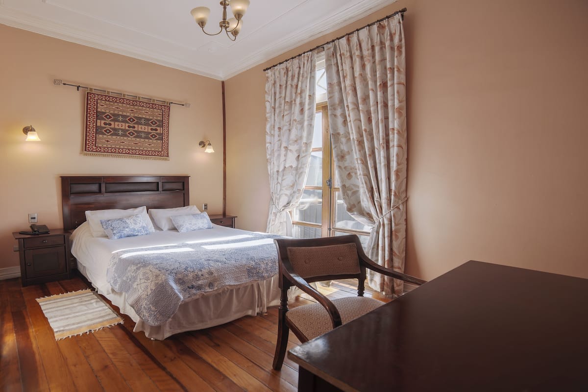 Un dormitorio con una cama grande, una mesita de noche de madera, un escritorio y una silla.