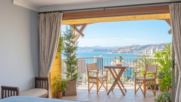 Une chambre avec un lit, un balcon avec une table et des chaises, et une vue sur la mer.