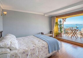 Un dormitorio con cama, mesita de noche, ventana con cortinas y vistas al exterior.