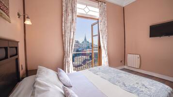 A bedroom with a large bed, a window with curtains, a mounted TV, and a radiator.