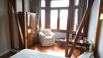 Un dormitorio con una cama grande, una silla, una mesita y una ventana con cortinas.