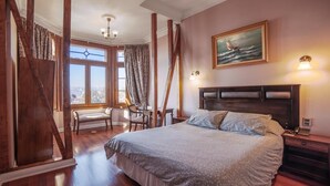 Une chambre spacieuse avec un grand lit, une tête de lit en bois, un bureau et une chaise. Il y a une fenêtre avec des rideaux et un tableau représentant un voilier accroché au mur.