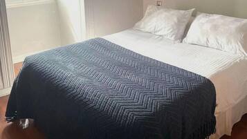 Un dormitorio con cama, ventana, lámpara de pared y un cuadro enmarcado.