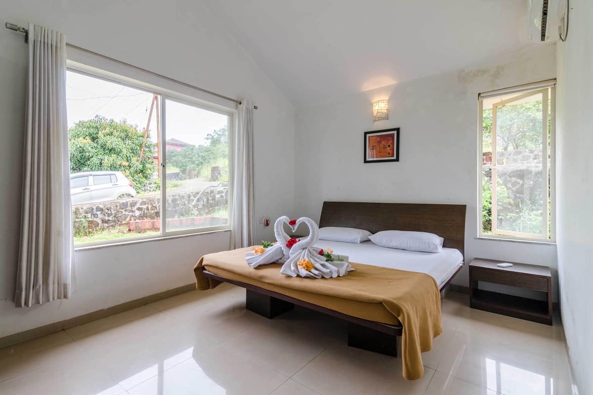 A hotel room with a bed, a bench with towels, and two windows.