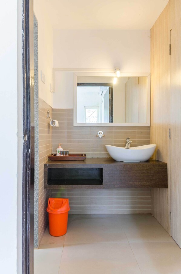Un baño moderno con lavamanos tipo recipiente, tocador de madera oscura, paredes con azulejos y un espejo sobre el lavamanos.