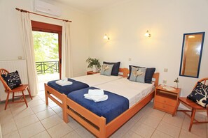 A double bed with blue and white bedding, two bedside tables, a chair, a small bedside table with a lamp, a potted plant, and a large mirror on the wall.