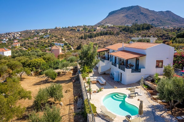 A modern villa with a swimming pool, surrounded by a landscaped garden and a view of a mountain.