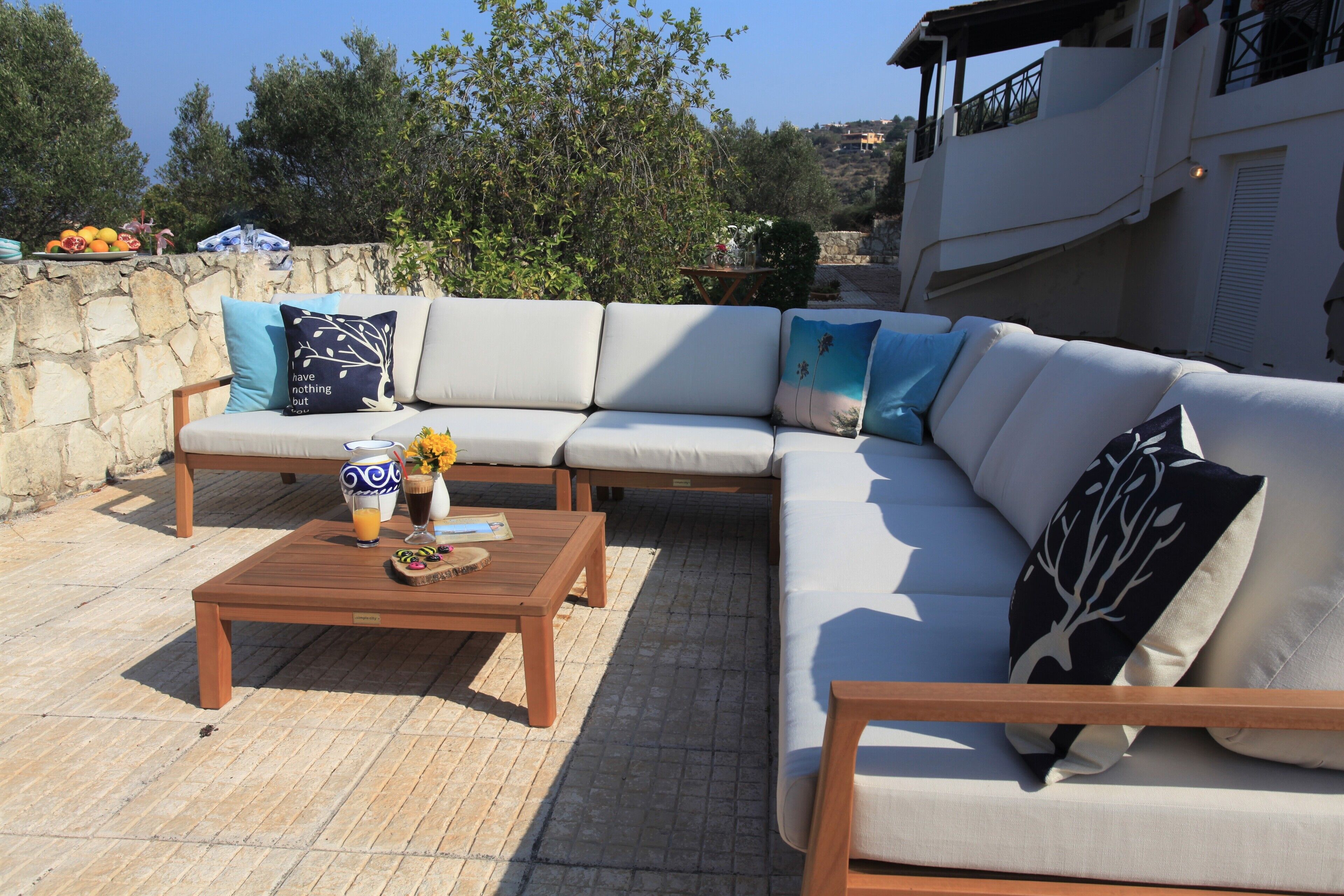 A sunlit outdoor seating area with a sofa, a wooden table, and a stone wall.