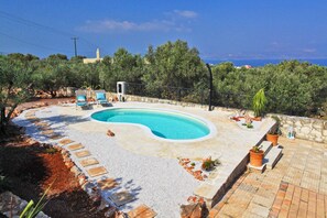 A swimming pool with a curved edge, surrounded by a stone deck and potted plants.