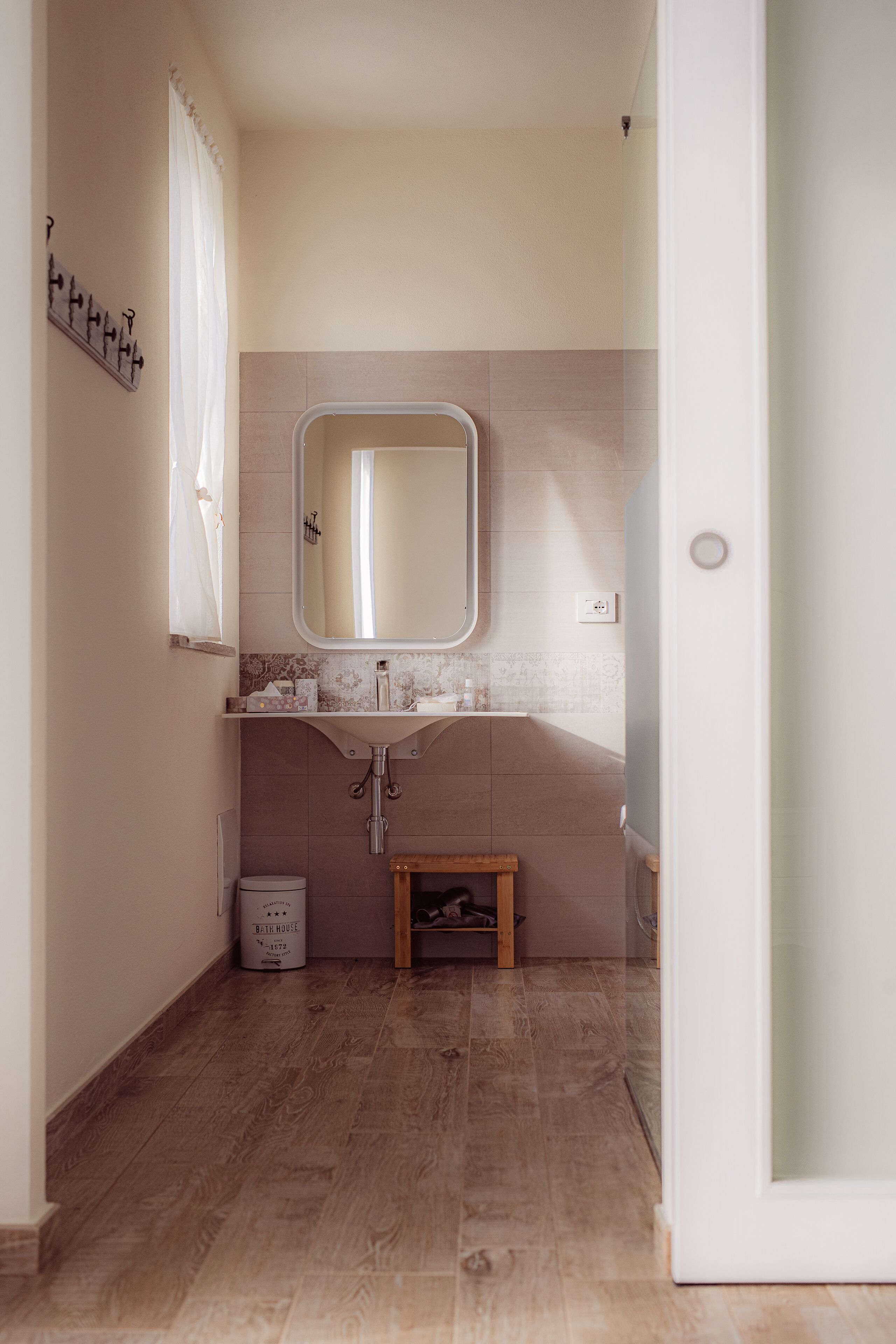 A bathroom with a wooden floor, a white sink with a mirror, and a small wooden stool.