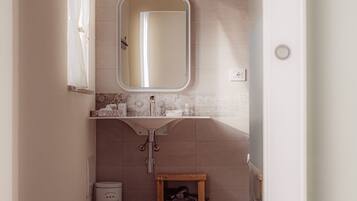 A bathroom with a wooden floor, a white sink with a mirror, and a small wooden stool.