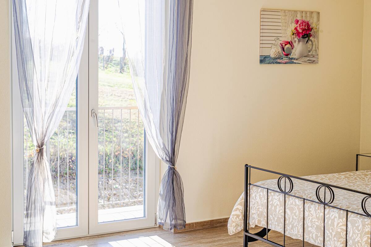 A bedroom with a bed, a window with curtains, and a painting on the wall.