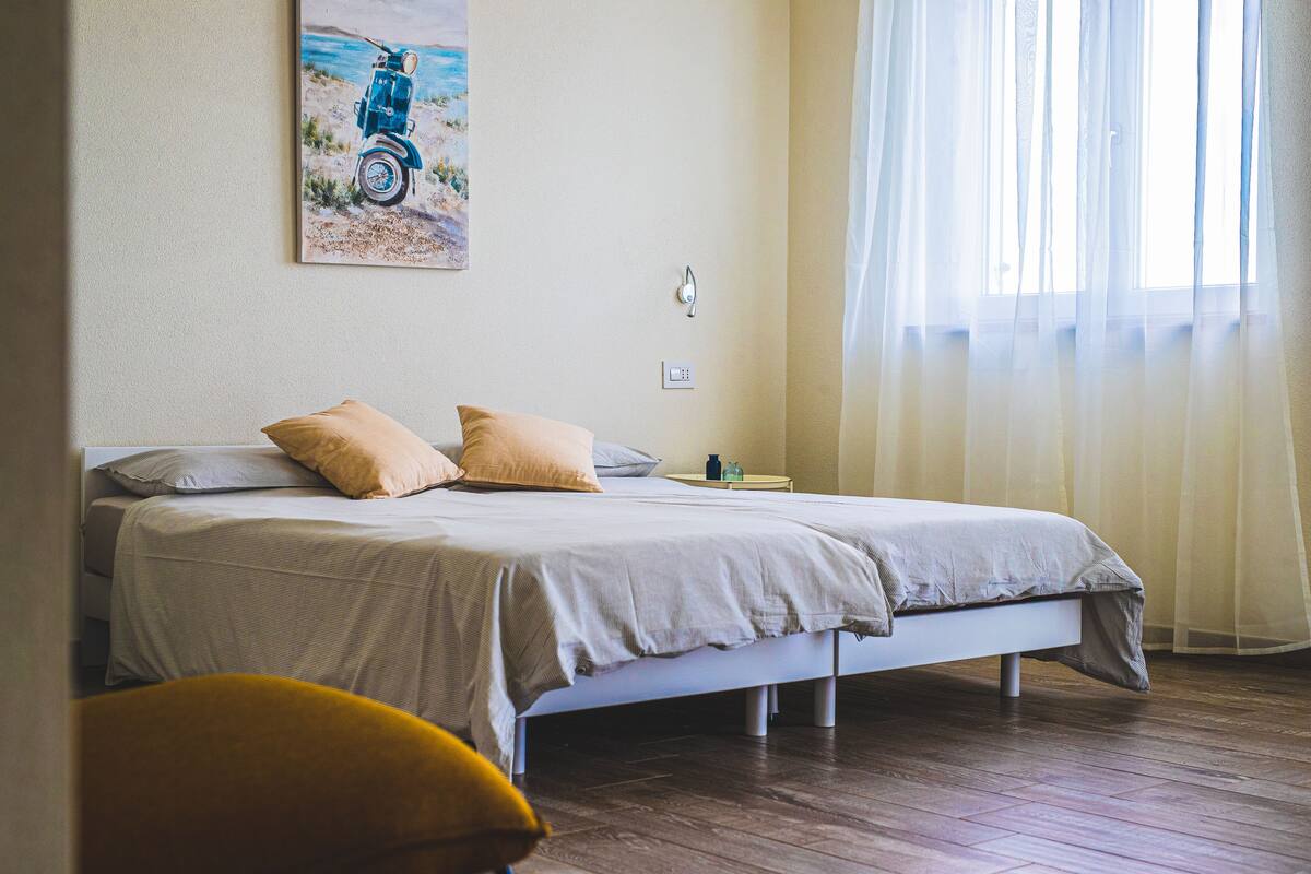 A bedroom with a bed, pillows, a nightstand, a lamp, and a painting on the wall.