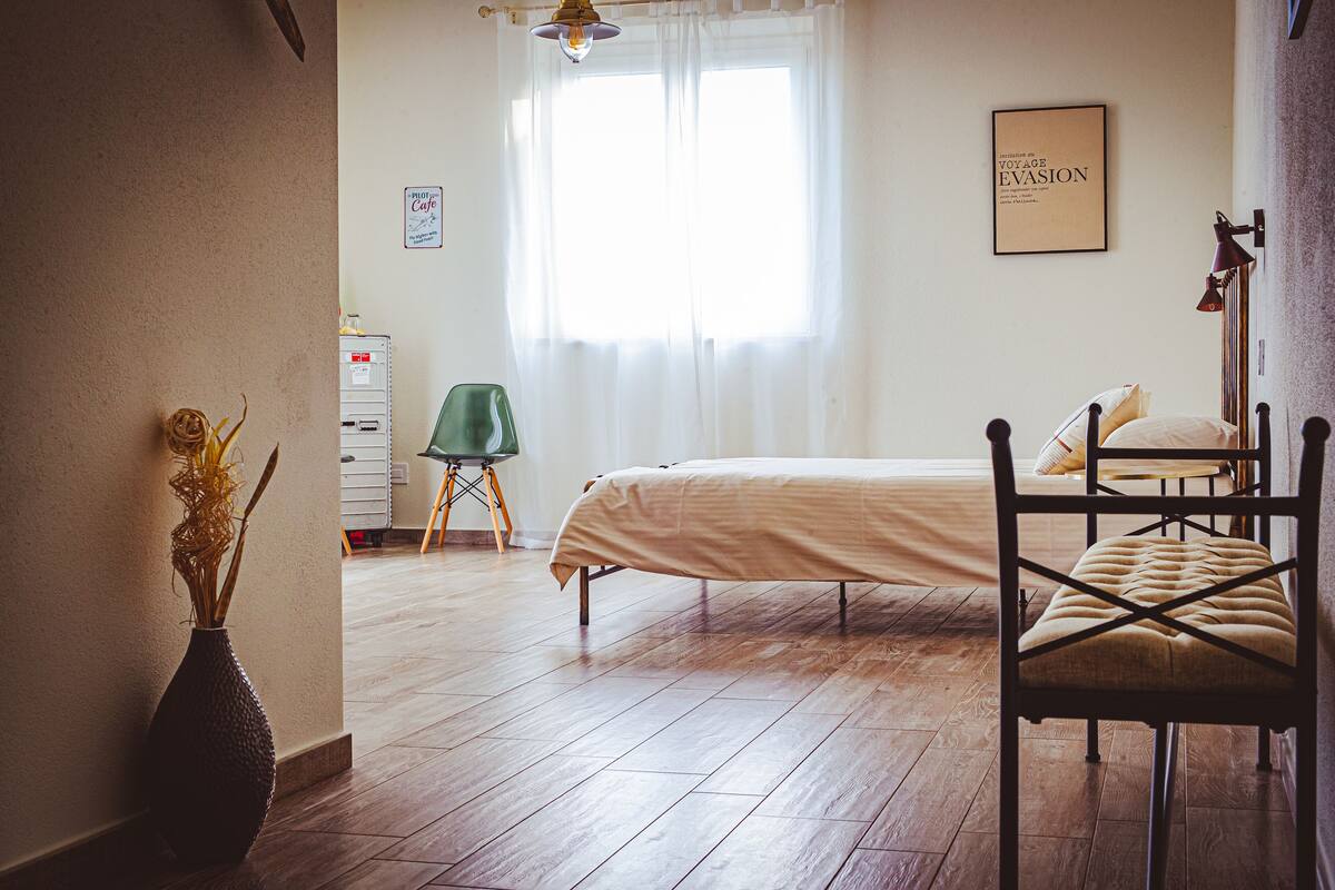 A bedroom with a bed, a chair, a desk, a lamp, and a vase.